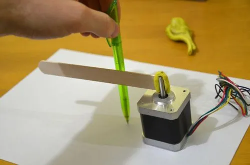 A photo of a popsicle stick stuck to the shaft of a stepper motor and it is being used as a ruler.