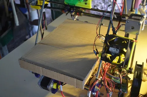 A photo of a cardboard cosy installed on a 3D printers heated build platform.