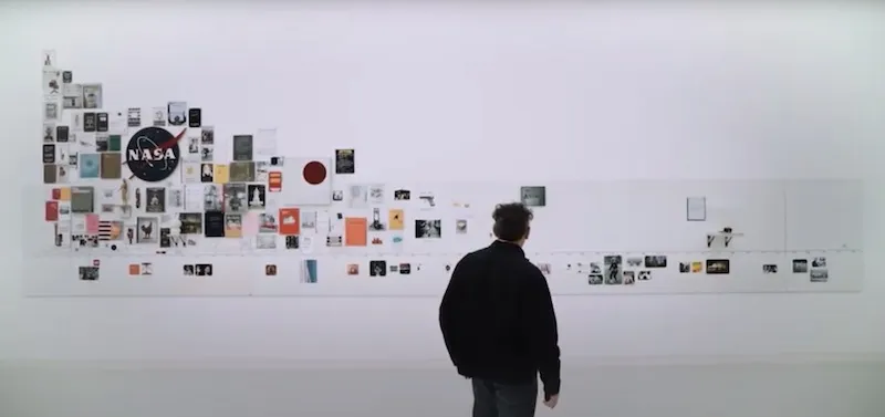 A picture of Tom Sachs standing infront of his timeline - a collage made from zines and other objects he has made.