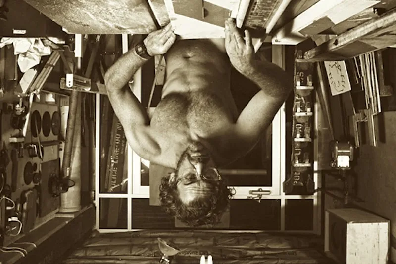 A photo of Tom Sachs, naked at a table-saw. The photo is upside down and has a sepia colour filter.